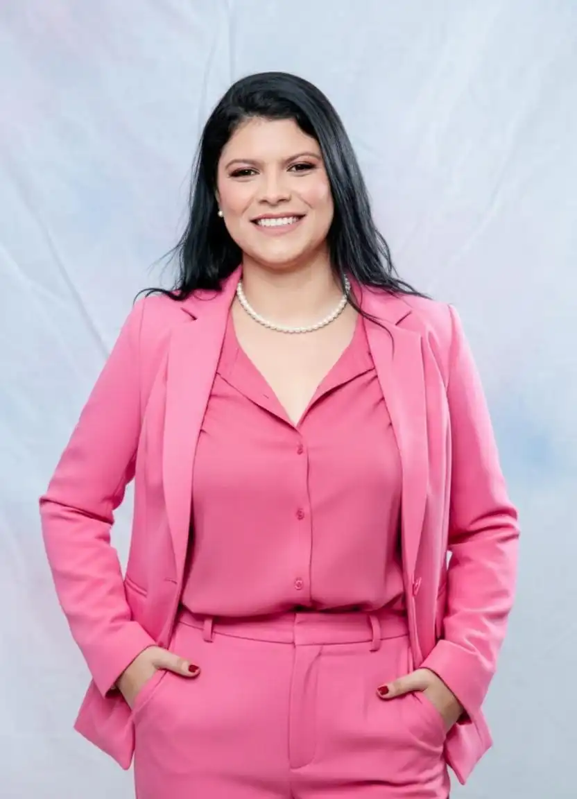Dra. Taíni Santos Silva, advogada trabalhista em Alfenas/MG, sorrindo com roupa rosa profissional.